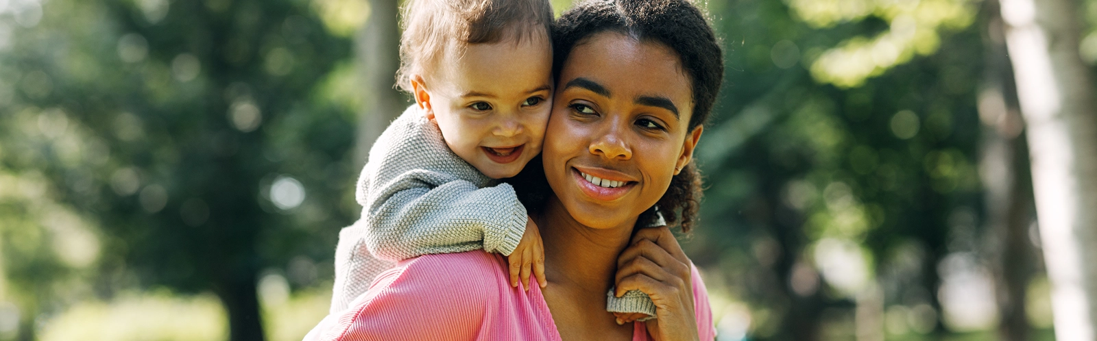 smiling-mother-carrying-baby-girl-back-park