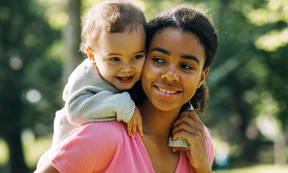 smiling-mother-carrying-baby-girl-back-park